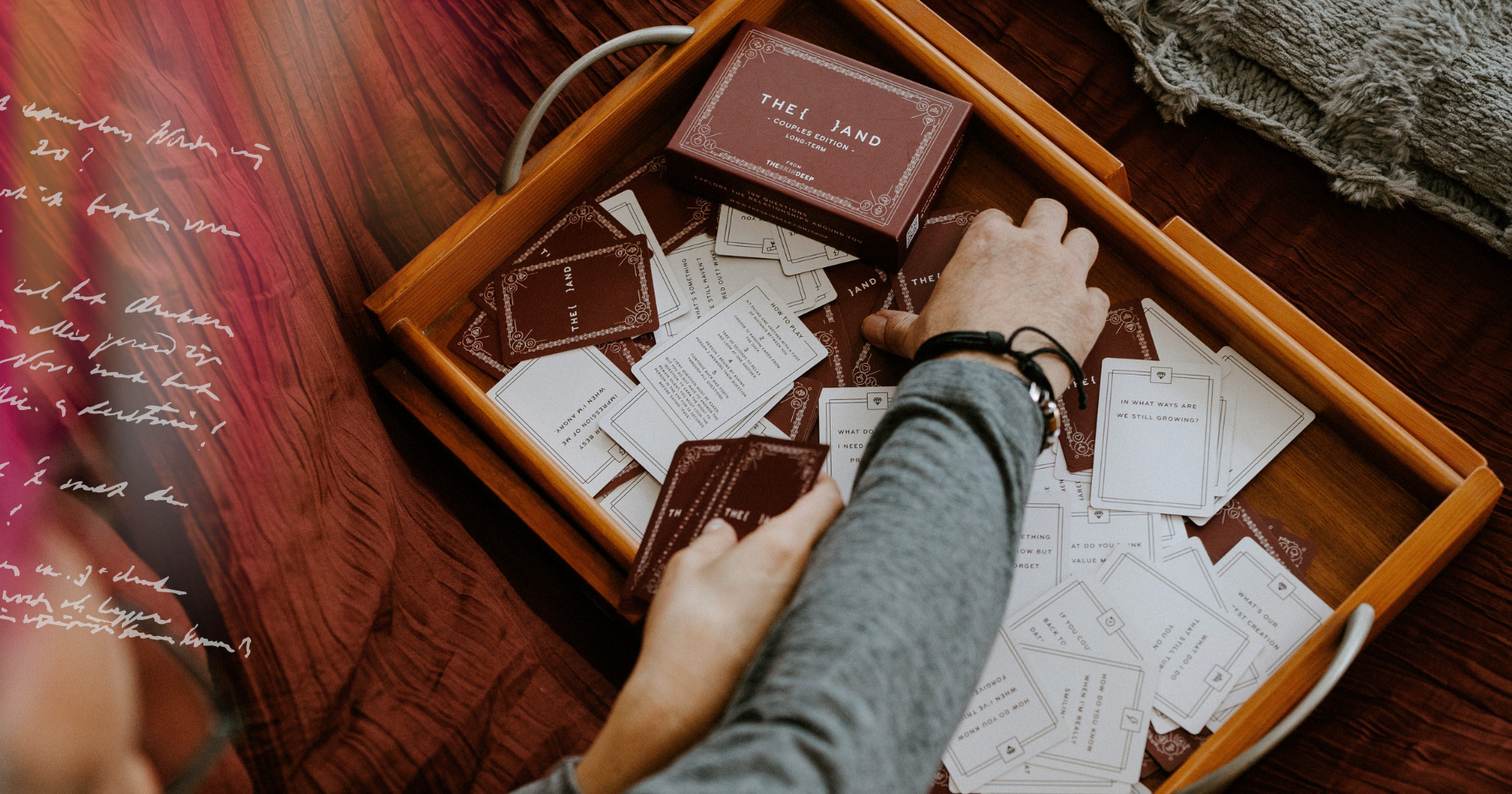 Picture of a card game in a wooden tray and hands reaching out for the cards.
