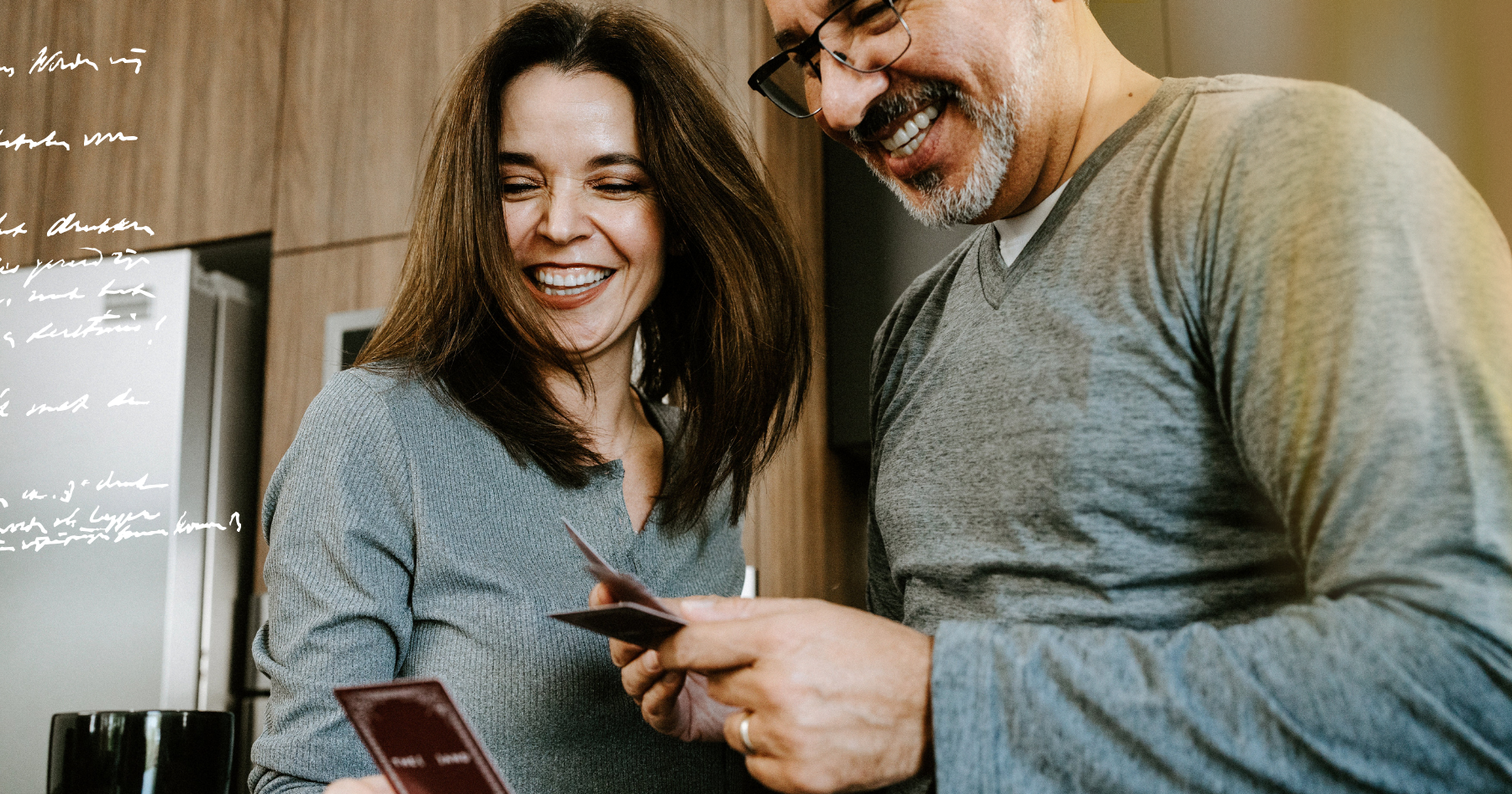 Picture of a couple playing a card game in the kitchen, wearing pajamas and laughing together