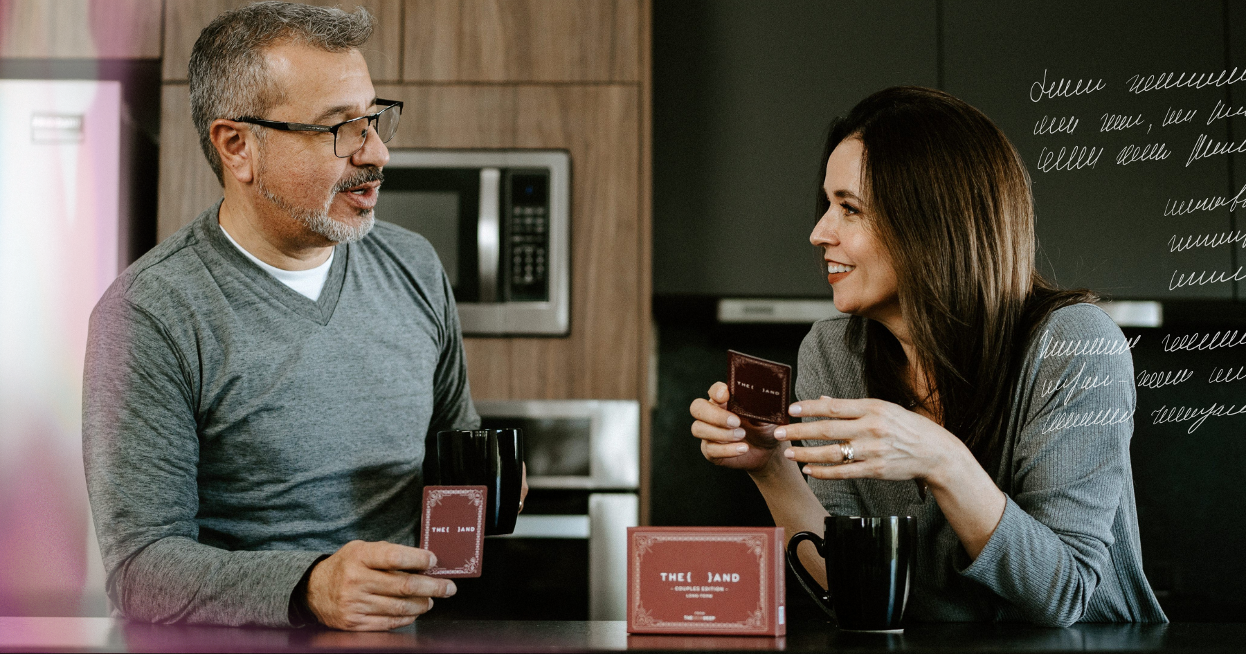Picture of a couple playing a card game in the kitchen, wearing pajamas and laughing together