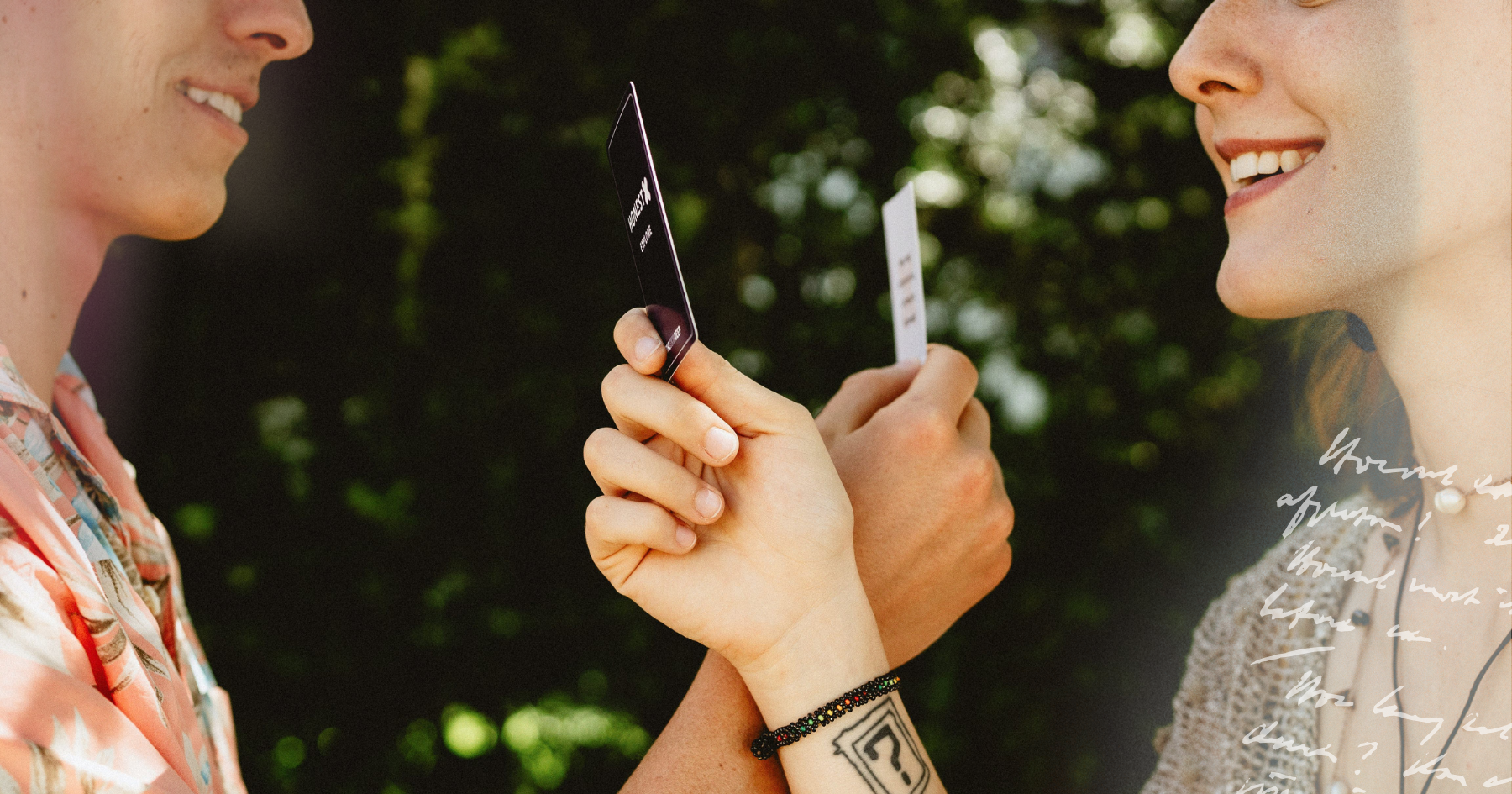 Picture of a couple playing a card game and smiling in front of bushes
