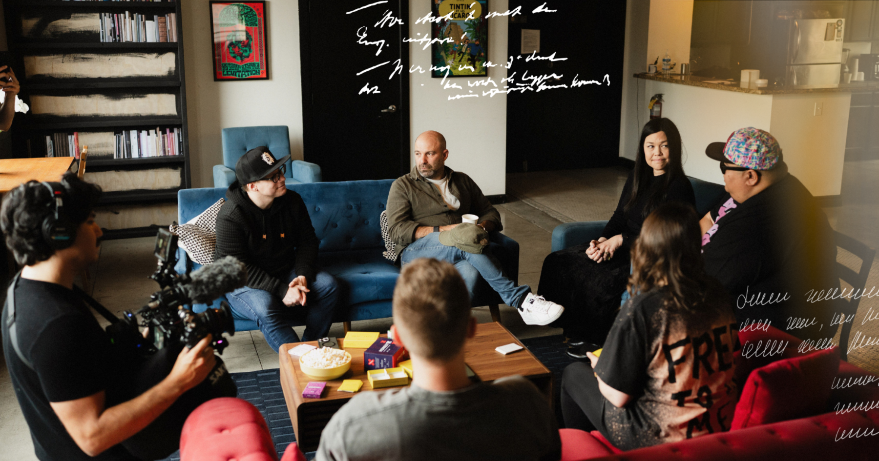A group of friends sitting down on blue and red couches and having a conversation, a camera recording them