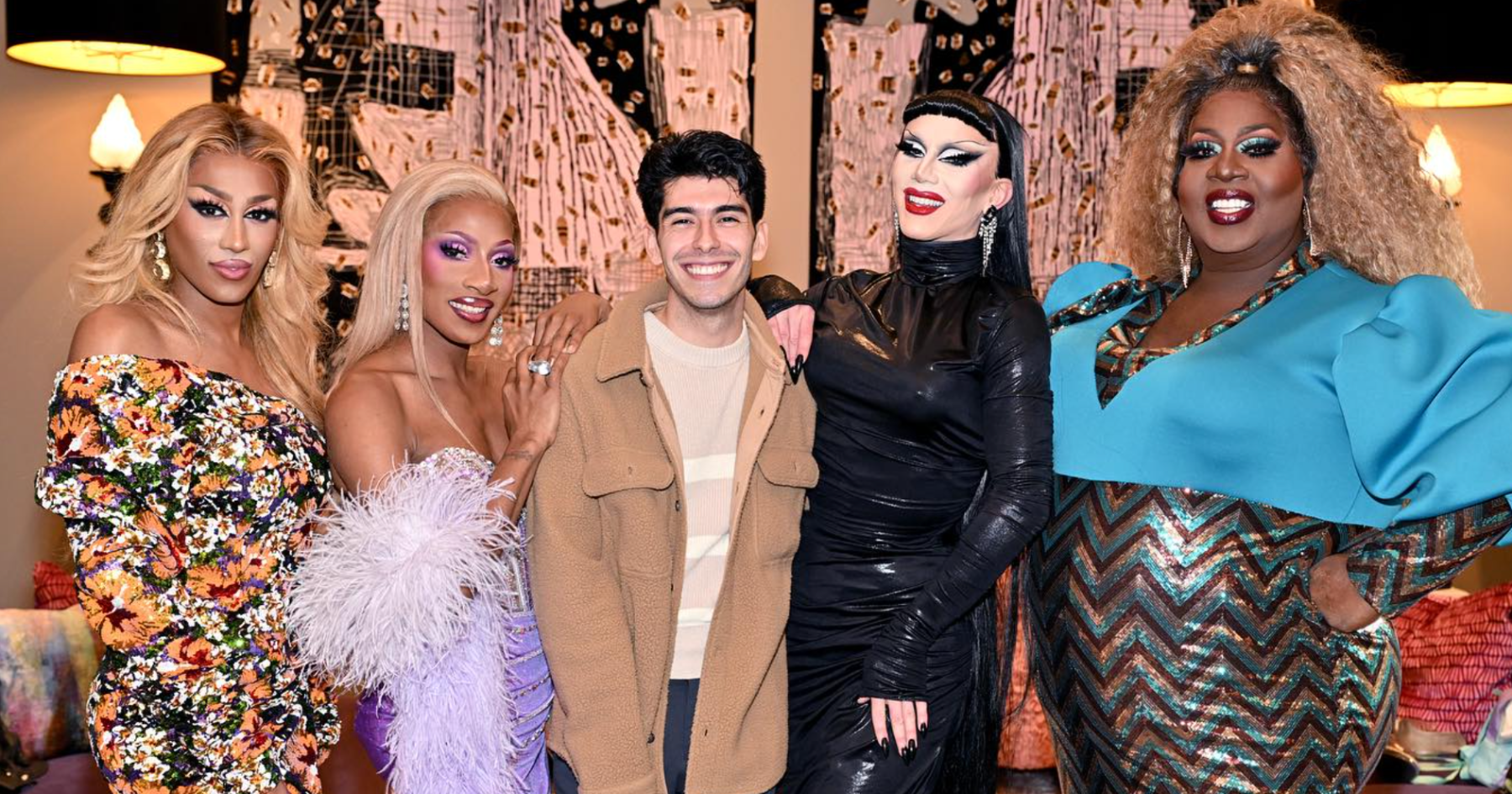 A guy hugging four drag queens in fabulous dresses