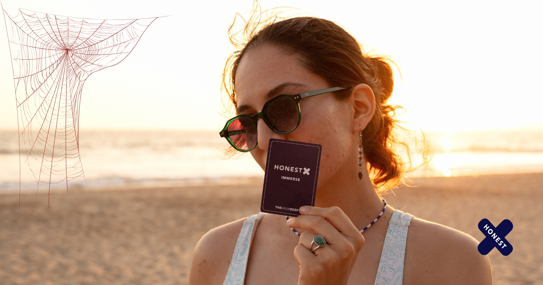 Picture of a woman at the beach holding a bunch of Honest X cards to her face covering her mouth