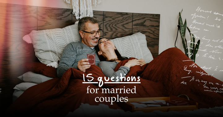 Picture of a couple laying in bed under the covers, playing a card game and laughing together