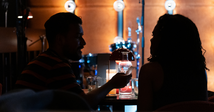 Two people in silhouette sitting across from each other at a table with drinks and warm lighting, engaged in intimate conversation at a Magiccal Moments event